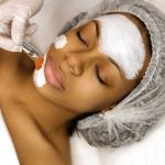 Application of a cosmetology mask on the face of a young afro american woman. Procedure for face skin rejuvenation. Beauty, spa, cosmetology and preservation of youth. Wellness relaxation concept.